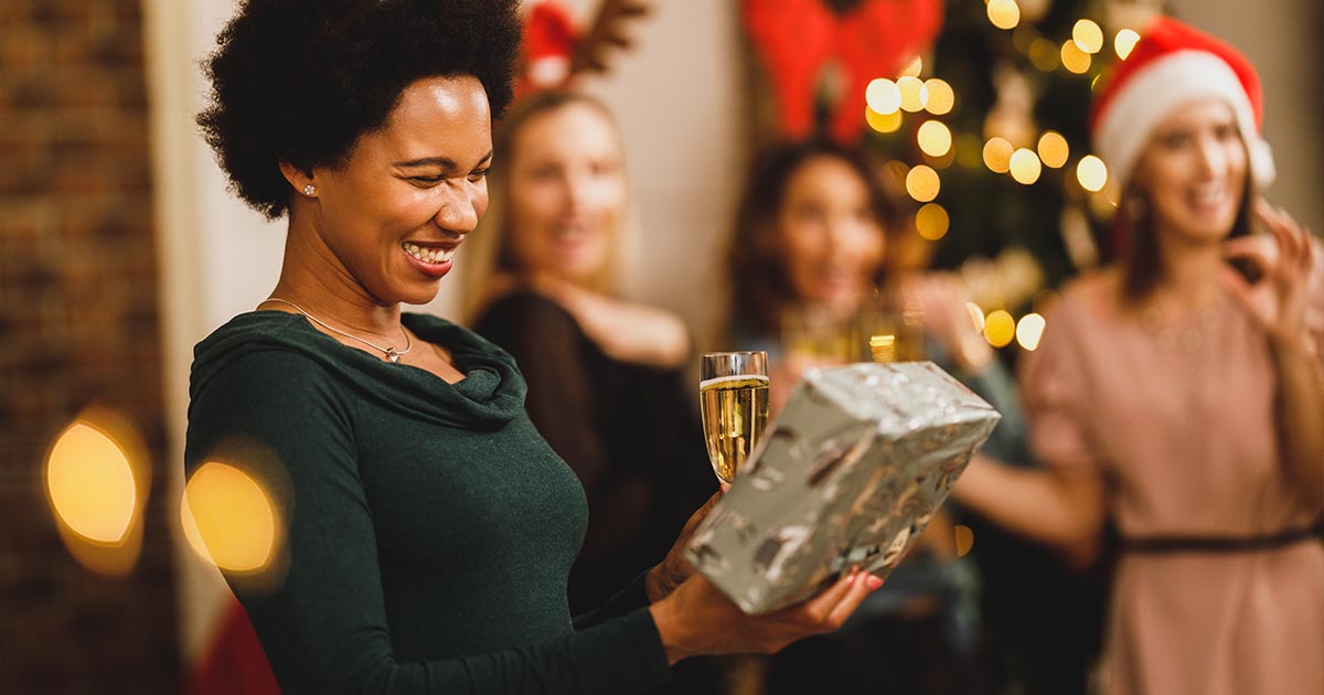 Woman holding silver wrapped present while holding a glass of champagne at holiday party