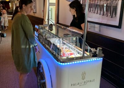 Woman serving gelato behind a gelato cart with Palais Royale logo on the side