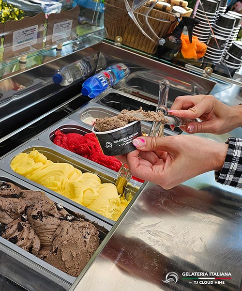 Close up of a Woman's hands scooping chocolate gelato into a branded cup over a Vintage Gelato Cart