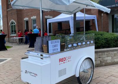 White Gelato Cart with "RedDay" logo on front with group of people behind